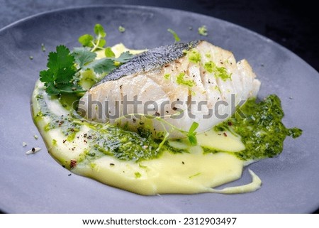 Modern style traditional fried skrei cod fish filet with mashed potato cream and coriander lime relish served as close-up on Nordic design plate with copy space 