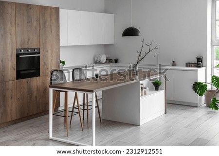Interior of modern kitchen with island, built-in oven and white counters Royalty-Free Stock Photo #2312912551