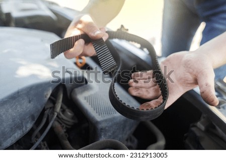 Timing belt break. Man near hood of car is looking for a malfunction due to which the engine does not work. Driver is holding a broken front belt in his hands. Shock due to irreparable damage. Royalty-Free Stock Photo #2312913005