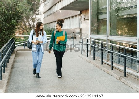 Two happy students girls walking and talking each other in University campus after classes