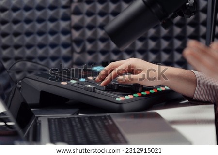 Crop woman adjusting controls of mixing console while sitting at table and recording podcast in studio