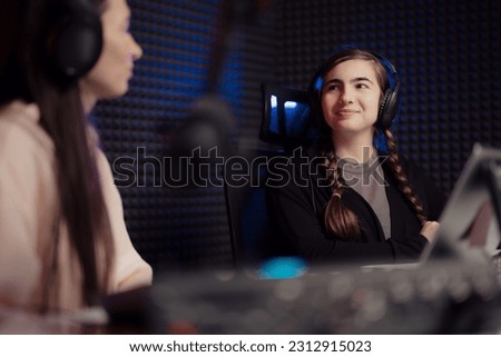 Women speaking during radio program in studio. Female host and guest sitting at table with equipment while broadcasting radio program in recording studio