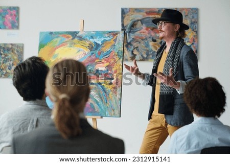 Artist presenting his picture to group of people at art exhibition in gallery