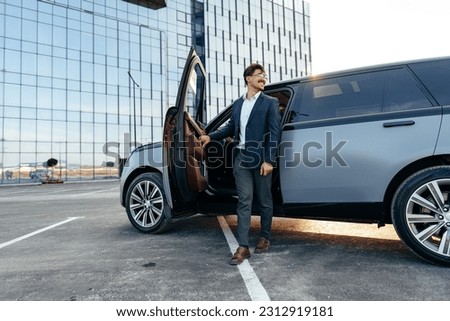Young handsome businessman in a suit comes out of the luxury car Royalty-Free Stock Photo #2312919181