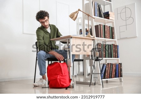 Male student with backpack sitting at table in library