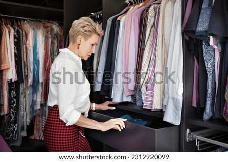 Mature woman chooses or organizes clothes and things in drawer in wardrobe closet dressing room at home. Royalty-Free Stock Photo #2312920099