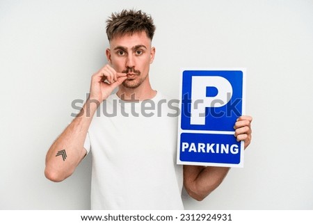 Young caucasian man holding parking placard isolated on white background with fingers on lips keeping a secret.