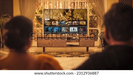 Back View of Elderly Indian Couple Watching TV while Sitting on a Couch in the Living Room. Relaxed Evening for Enjoying Favourite Movies, TV Shows, Content and Ads Thank to Streaming Online Service Royalty-Free Stock Photo #2312936887