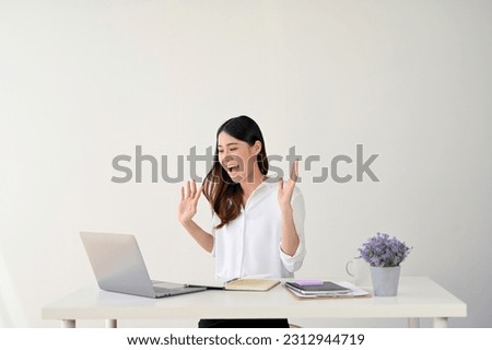 An excited young Asian businesswoman or female office worker looks at her laptop screen, receives good news by getting a job promotion letter through email, feeling shocked and surprised.