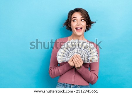 Photo of positive excited woman dressed pink shirt rising cash fan looking empty space isolated blue color background