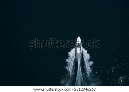 high speed white big boat with people moving fast on dark water leaving a white trail top view. Royalty-Free Stock Photo #2312946269