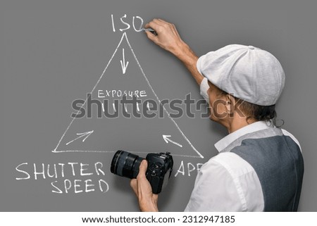 A professional male photographer teaches to take pictures, draws an exposure scheme, ISO aperture shutter speeds on a gray background