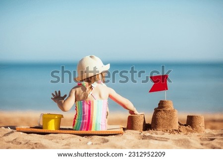 baby child in hat sits on beach against background of sea and plays sand, builds castle. vacation with kids in sunny summer.