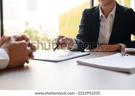 Female real estate agent in suit negotiating about house price, finance, and agreement with buyer or client at desk showing document detail and information before signing contract. Business, mortgage