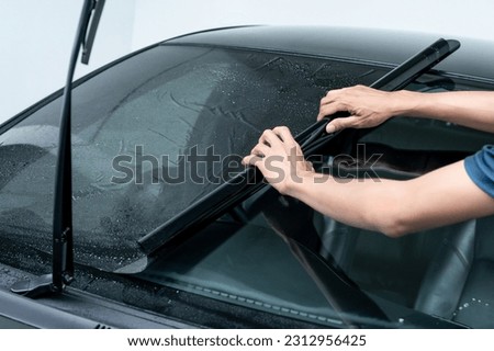 Male auto specialist worker hand rolling car window film on front windscreen glass surface. Car side window film removal and tinting installation.  Royalty-Free Stock Photo #2312956425