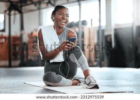 Phone, earphones and funny black woman in gym for fitness, sports or exercise. Smartphone, music and African female athlete laughing at web meme or comedy on break after workout, training or pilates. Royalty-Free Stock Photo #2312975539