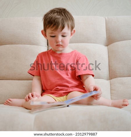 The cute baby is playing with the colorful picture book, flipping through the pages and touching the pictures. The little child is lost in thought as he reads book while sitting at home.