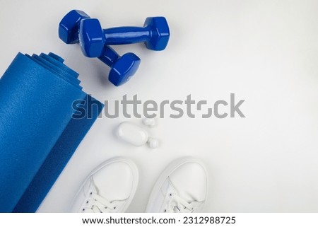 Fitness accessories concept. Photo of dumbbells, smartphone with headphones white sneakers sports mat on a white background with empty space.