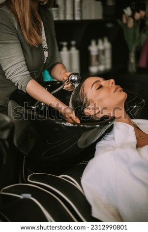 Close up of hairdresser washing her clients brown hair with water on the washing sink at the hair salon