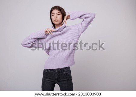 Fashion photo of a beautiful elegant young asian woman in a pretty pale purple, lilac, lavender sweater, blouse, black jeans, denim posing on white, soft gray background. Studio Shot. Slim figure. 