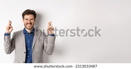 Motivated and excited businessman smiling positive, look hopeful and cross fingers for good luck, making wish, waiting for announcement, white background.