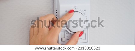 Woman hand adjusts or turns on wall temperature controller controller button Royalty-Free Stock Photo #2313010523
