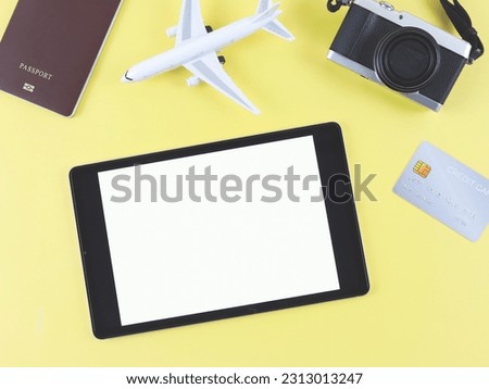 Top view or flat lay of digital tablet with blank white screen, airplane model, passport, credit card and digital camera isolated on yellow background. travel planning concept.