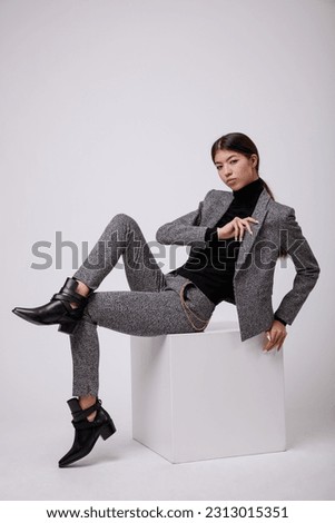 Fashion photo of a beautiful elegant young asian woman in a pretty gray suit, pants, trousers, jacket, blazer, black top posing over white, soft gray background. Studio Shot, portrait. Slim figure