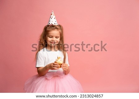Happy little girl in party cap for her birthday makes wish and blows out candle on cake