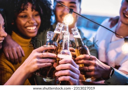 Multiracial friends toasting beer bottle at rooftop party - Young people having fun together outside - Food and beverage life style concept with guys and girls drinking alcohol on summer open bar Royalty-Free Stock Photo #2313027019
