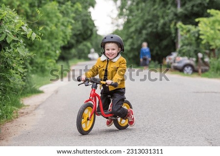 A cheerful little boy rides a running bike in a helmet outdoors. A happy child is engaged in an active sport. Protection. Life insurance and child safety. Royalty-Free Stock Photo #2313031311