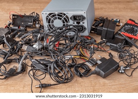 Pile of old wires, connections, headphones and chargers on a wooden table close-up. Replacement of old elements and parts of electronic devices. Repair of broken electronic devices and their elements. Royalty-Free Stock Photo #2313031919