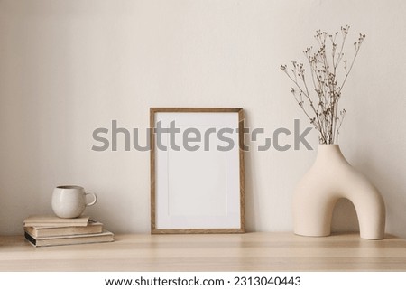 Elegant boho still life. Modern vase with dry grass on table, desk. Empty wooden picture frame mockup. Cup of coffee, books. Artistic poster display. Minimal home interior. Home office desk.