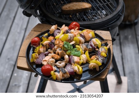 ready to eat - grilled shrimps with salmon and vegetables on a black plate, from a bbq grill at a summer day on the balcony