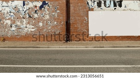 Brick wall covered with ripped billboards except one blank on the right.  Sidewalk and urban street in front. Grunge background for copy space.