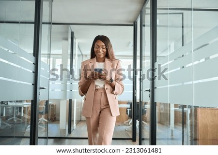 Young happy elegant busy professional African American business woman company executive manager worker wearing suit using cell phone walking in office hall holding mobile phone and working. Royalty-Free Stock Photo #2313061481