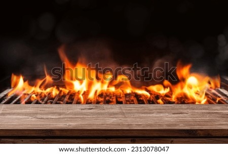 barbecue BBQ grill with flaming fire and ember charcoal on black background, wooden table Royalty-Free Stock Photo #2313078047