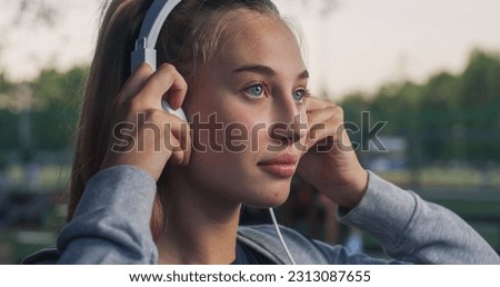 Closeup Portrait of Beautiful White Woman Smiling While Putting on her Headphones in the Park During her Early Morning Walk. Female Teenager Enjoying Music and Fresh Air While Being Outdoors Royalty-Free Stock Photo #2313087655