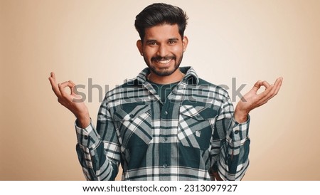 Keep calm down, relax, inner balance. Young indian man breathes deeply with mudra gesture, eyes closed, meditating with concentrated thoughts, peaceful mind. Hindu guy isolated on beige background