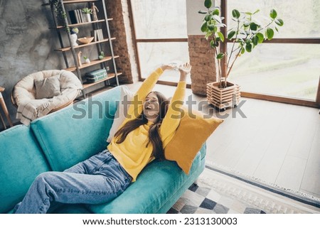 Photo of carefree overjoyed young person laying cozy couch stretch arms laugh have good mood chilling house inside