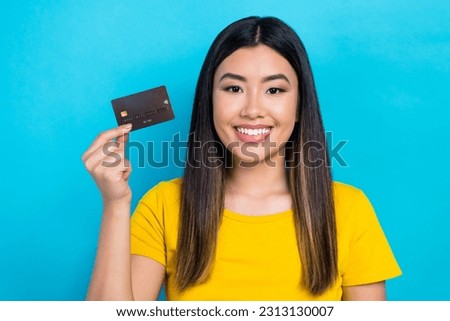 Photo of optimistic cute girl with straight hairdo dressed yellow t-shirt fingers hold plastic card isolated on blue color background