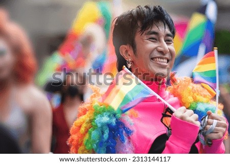 LGBTQ man having fun celebrate pride with flags at the annual Pride Parade, holding rainbow flags in two hands, celebrating LGBT pride month parade   Royalty-Free Stock Photo #2313144117