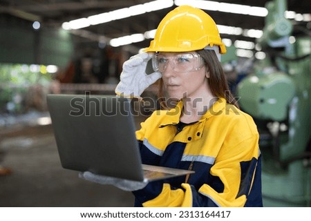 Factory female worker. Engineer woman worker with laptop working in plant production checking and testing machine in smart factory wearing yellow hard hat safety first at mechanic factory.