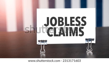 JOBLESS CLAIMS sign on paper on dark desk in sunlight. Blue and white background Royalty-Free Stock Photo #2313171603