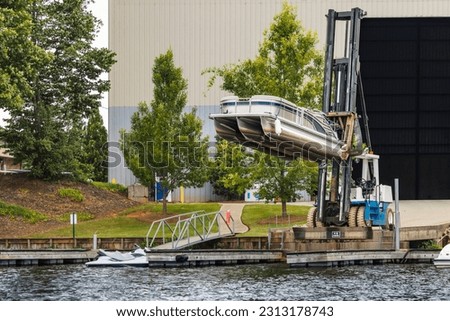 Pontoon boat removed from dry dock marina storage resting on fork lift ready for launch. Royalty-Free Stock Photo #2313178743