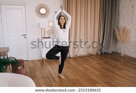 Full length of woman standing in Tree pose practicing yoga leading healthy lifestyle preparing body for childbirth during morning training in light apartment Royalty-Free Stock Photo #2313180631
