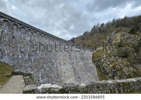 View of a huge, stone dam wall with no water and steps leading down to the base and surrounding craggy rocks 
