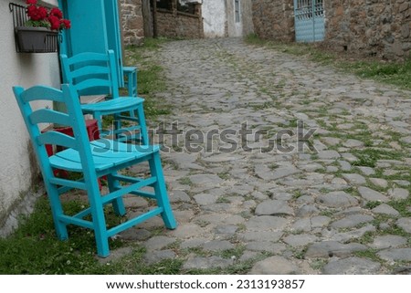 Blue chairs and wooden red stool against a home wall in Gliki, an old Greek village in Gokceada. Canakkale, Turkey. There's a flower pot with red flower on the small stool table