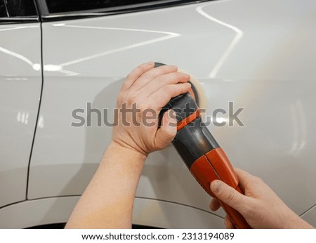 A car service worker polishes the car body with a polishing machine. Detailing and polishing of the car. Car detailing - hands with an orbital polishing machine in an auto repair shop.Selective focus.