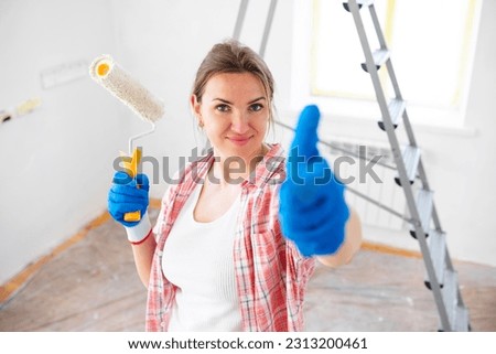 Beautiful woman with roller painter showing thumb-up while doing repair in room